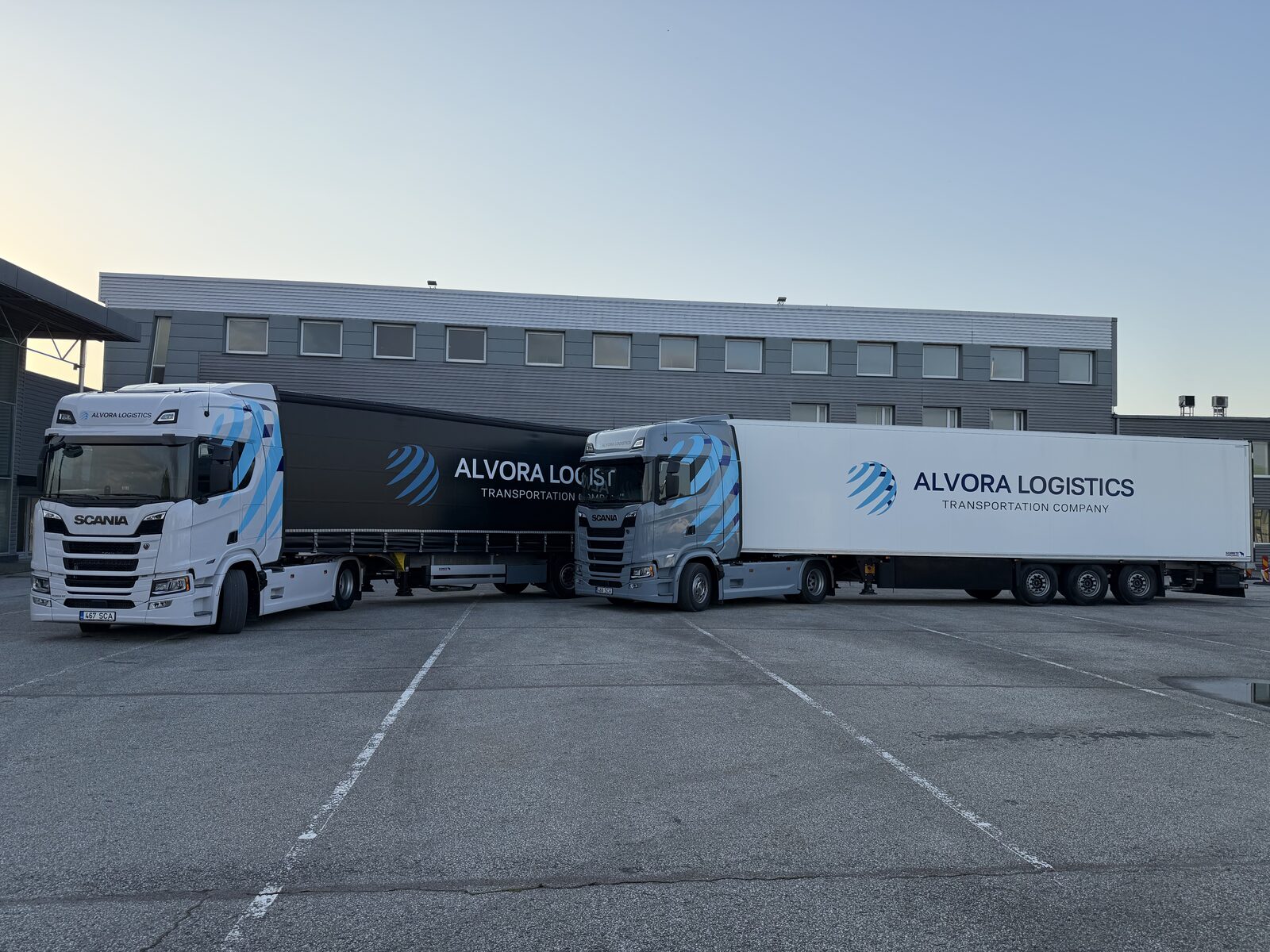 Two Alvora Logistics trucks and trailers parked at the depot at dusk