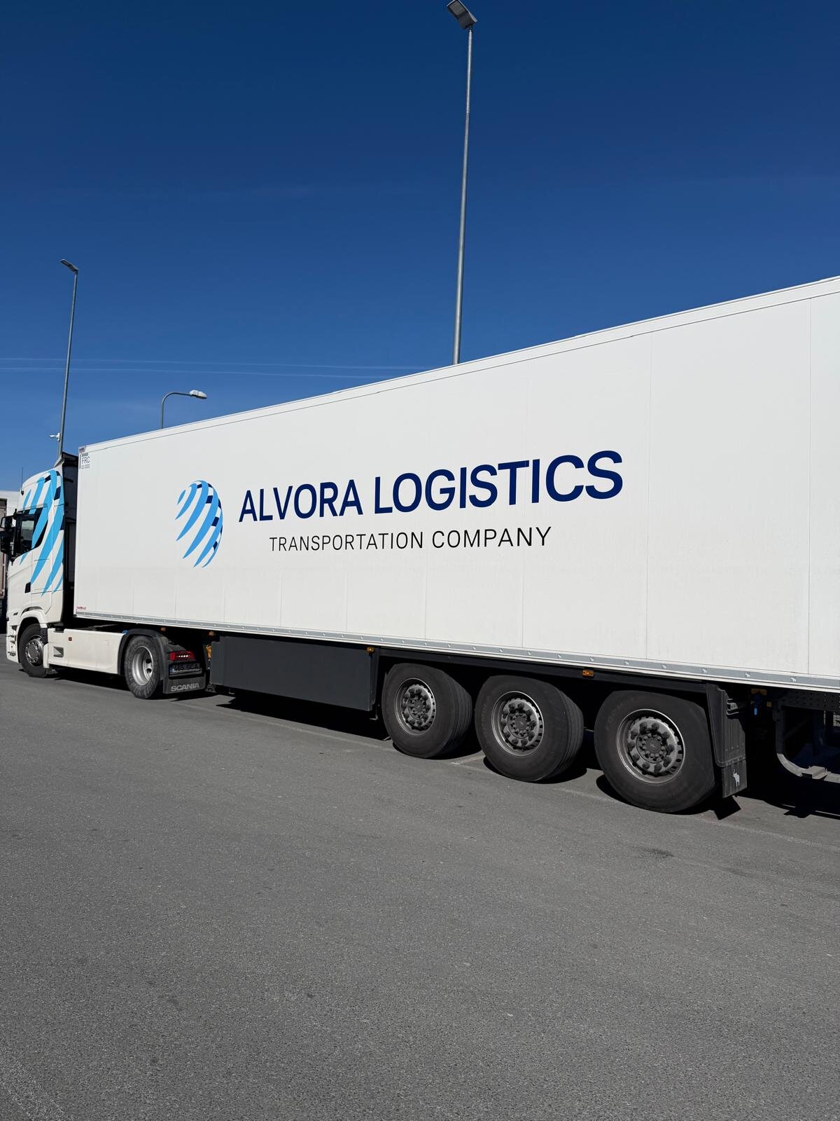 Alvora Logistics white hard-sided refrigerated trailer, side view on a clear sunny day